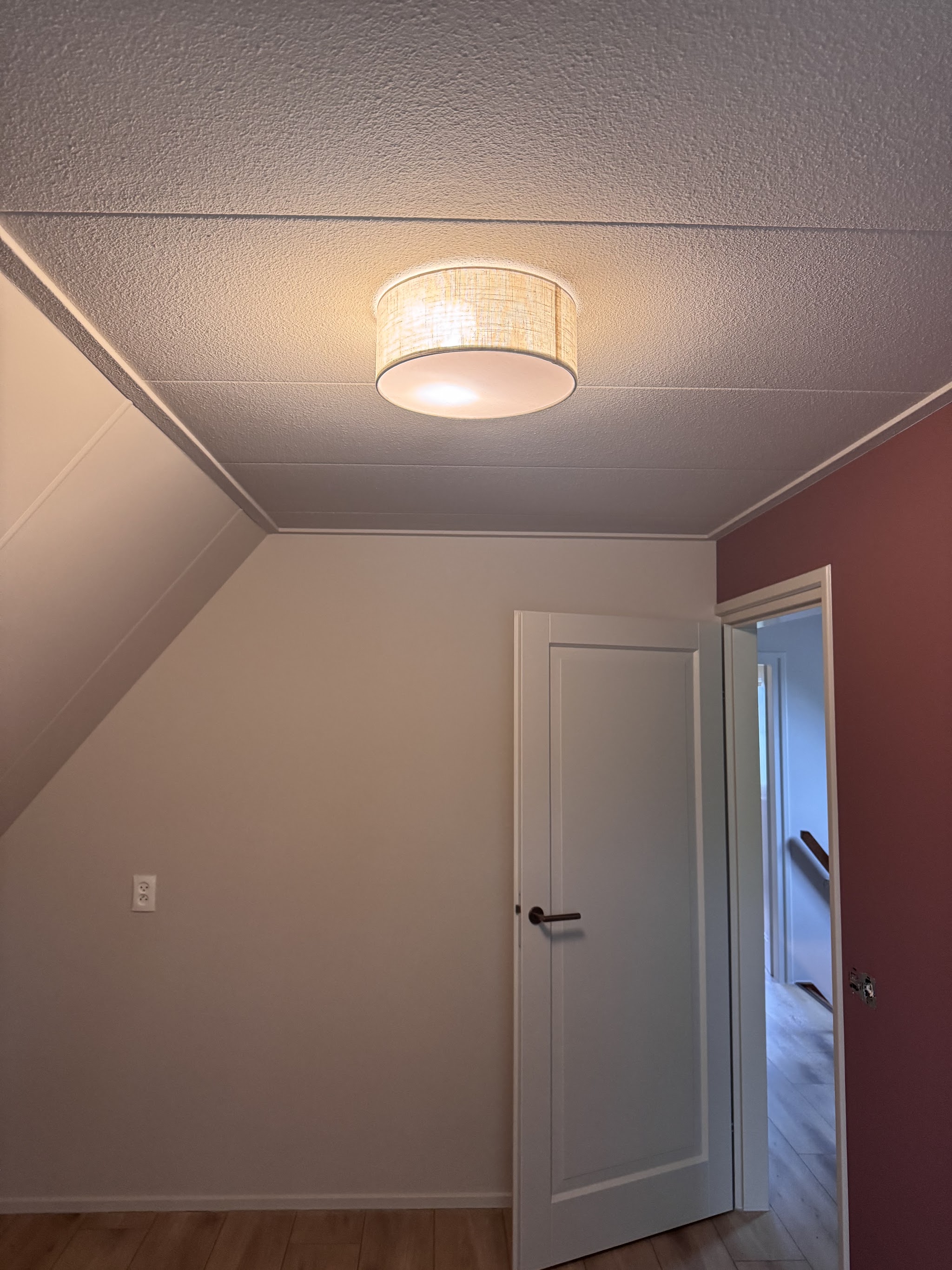 Afgewerkte zolderkamer met wit plafond, witte deur en een roze accentwand